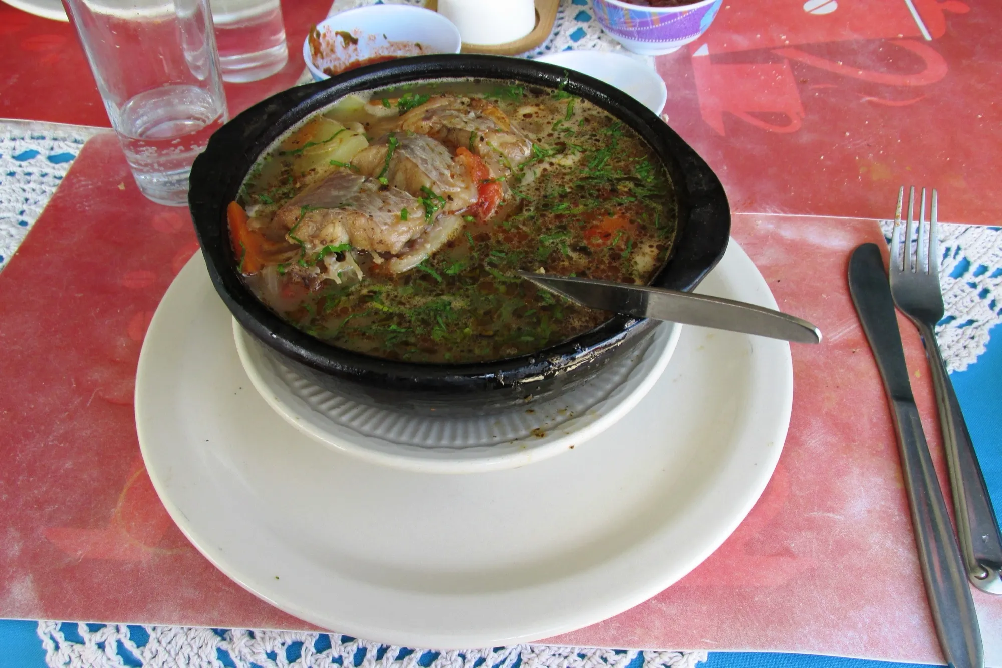 Caldillo de congrio servido en una olla negra sobre un plato, en una mesa con mantel rojo