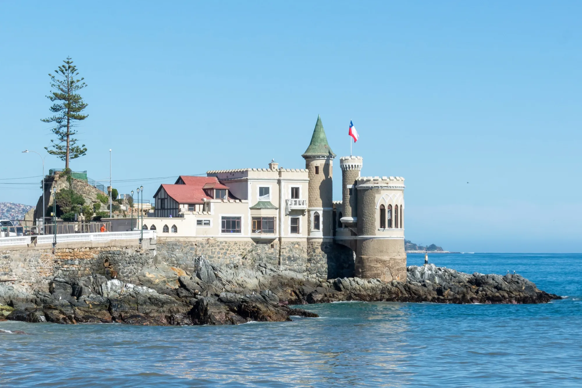 Castillo Wulff sobre un roquerío frente al mar, con una torre de techo verde y una bandera chilena