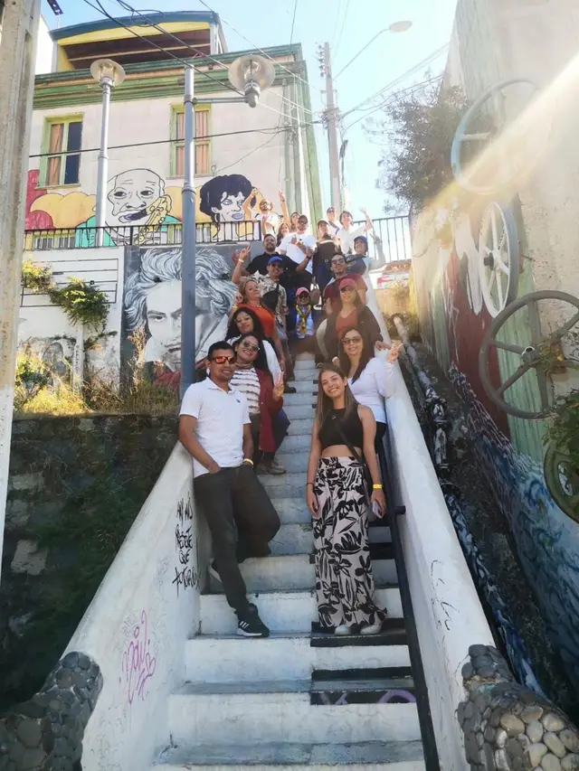 Grupo de viajeros en una escalera blanca junto a murales con retratos, en los cerros de Valparaíso