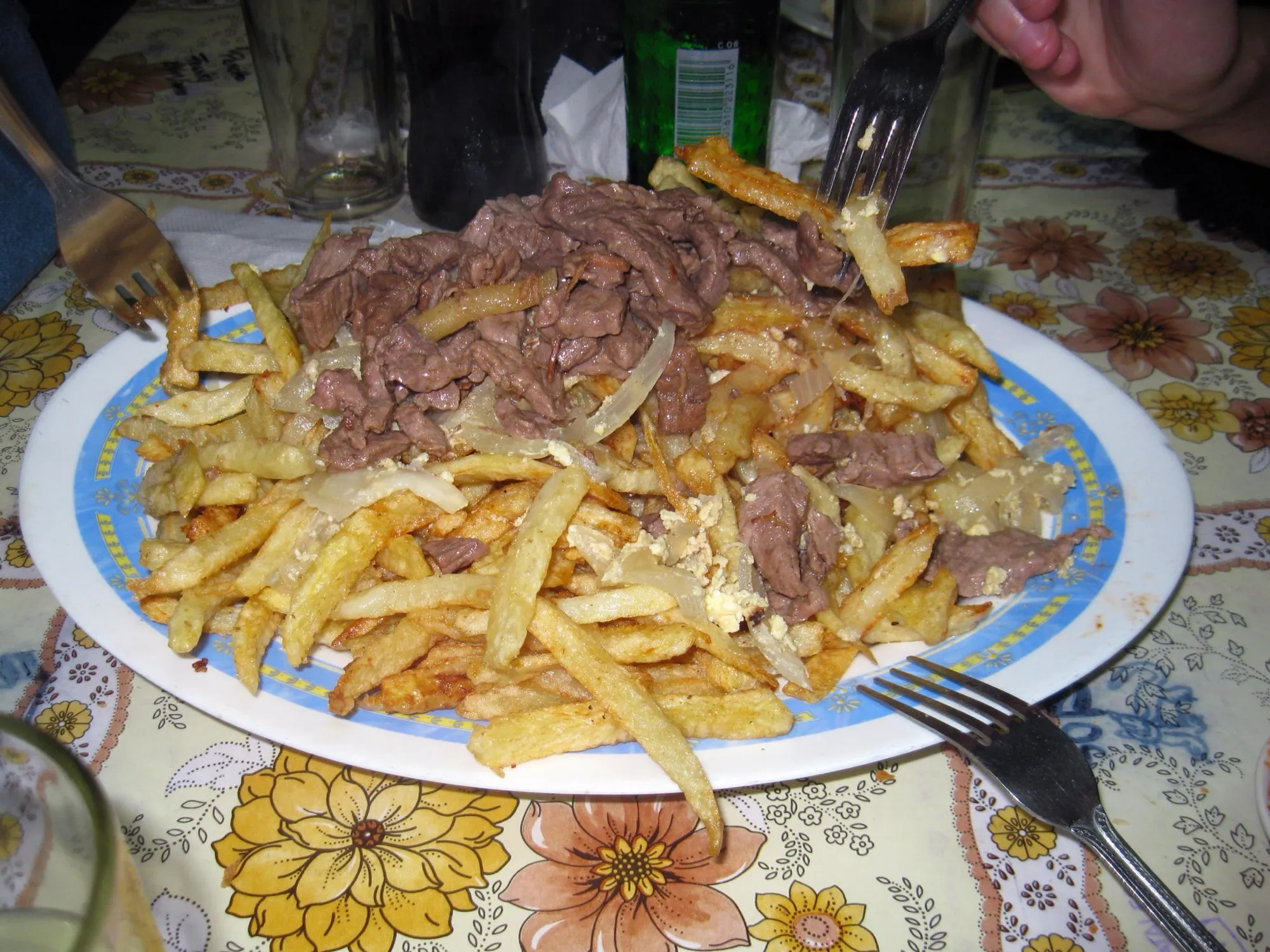 Fuente de papas fritas con carne en tiras sobre un mantel de flores