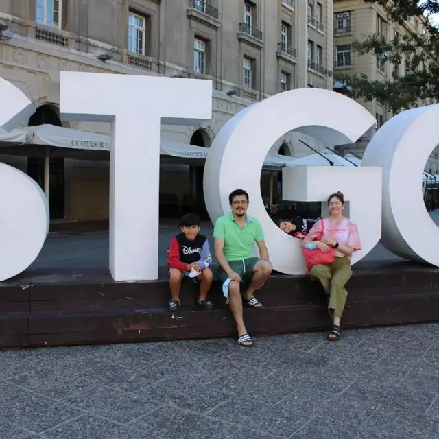 Visitantes sentados junto a las letras gigantes STGO en el centro de Santiago