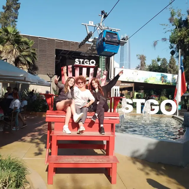 Grupo en la silla roja gigante con las letras STGO y el teleférico detrás
