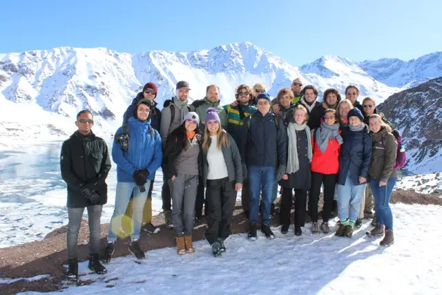 Grupo grande de viajeros posando en la nieve junto al embalse