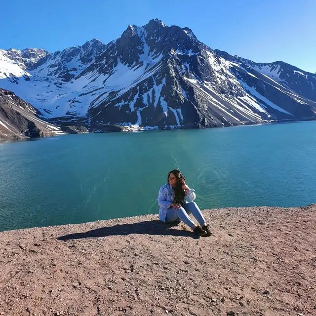 Viajera sentada frente a las aguas turquesa del Embalse El Yeso y los picos nevados