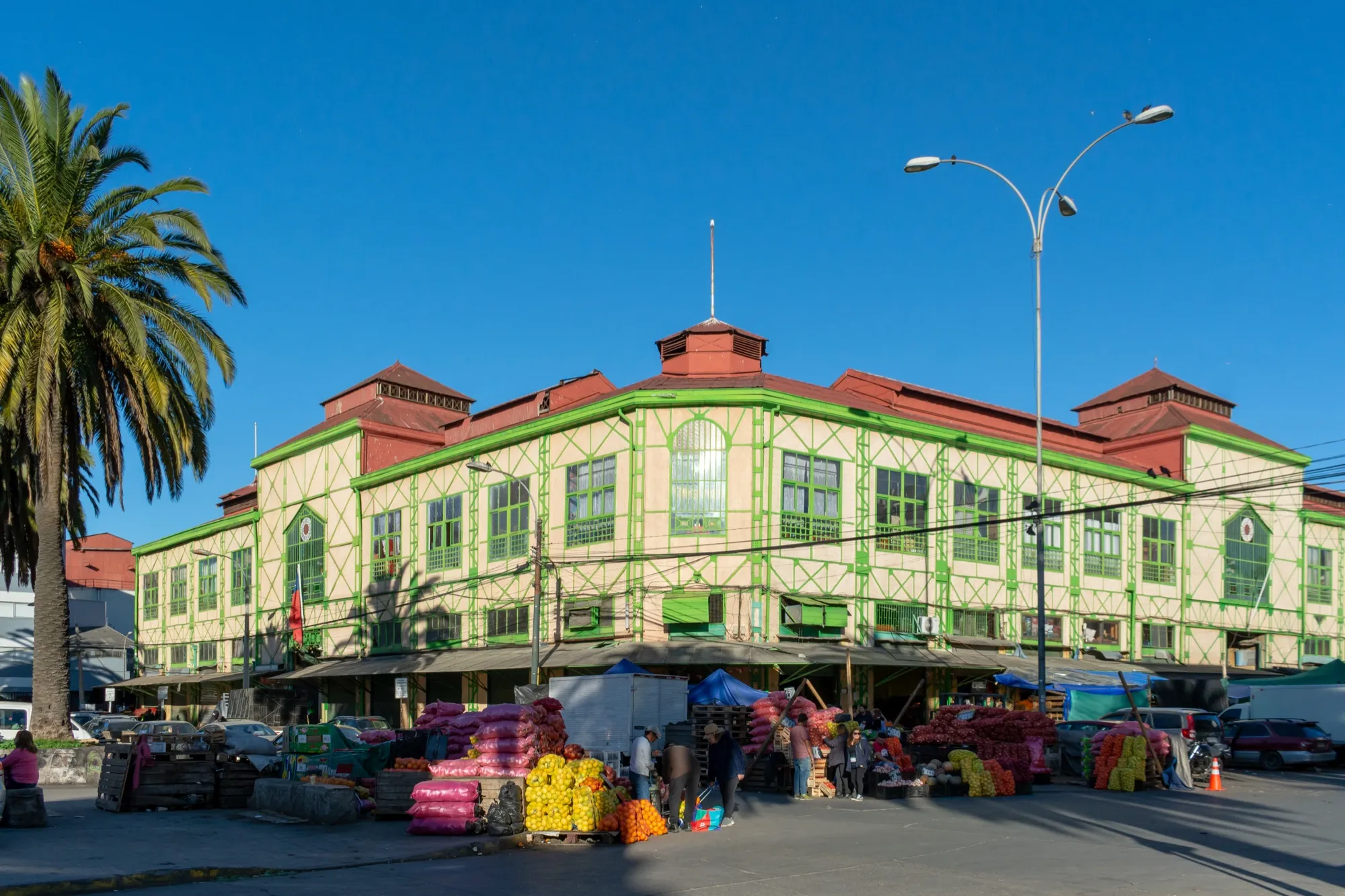 Fachada del Mercado Cardonal, un edificio verde y blanco con tejado rojizo, con puestos de frutas y verduras en la calle