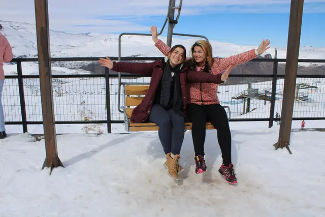 Dos amigas en un telesilla con los brazos en alto sobre la nieve