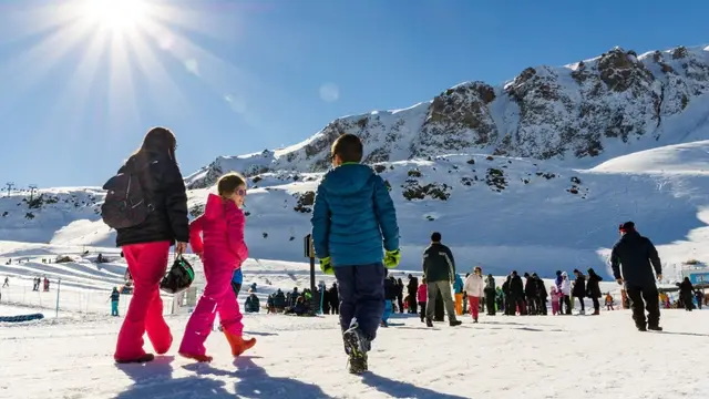 Familia caminando por la nieve con el sol y la cordillera de fondo