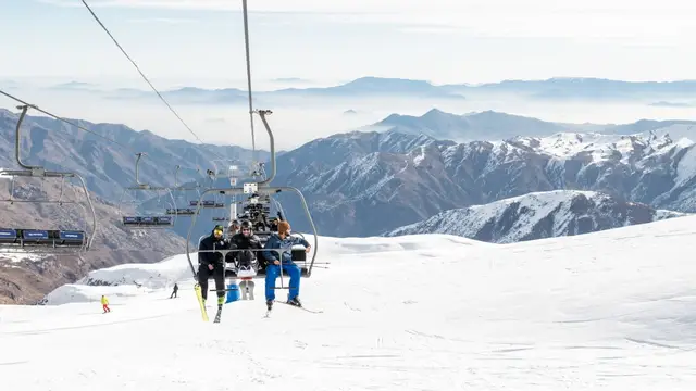 Telesilla con esquiadores sobre las pistas y la cordillera nevada