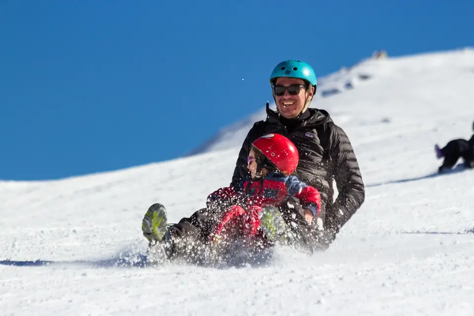 Familia bajando en trineo por la nieve en el Parque Farellones