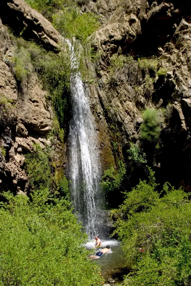 Cascada entre rocas y vegetación en la precordillera de Santiago, con dos personas bañándose en la poza