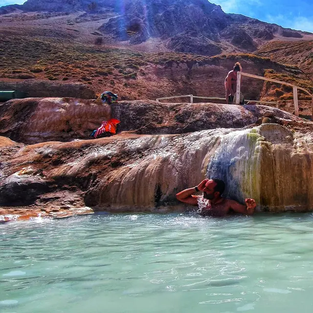 Viajero bajo una pequeña cascada de travertino en las aguas turquesa de las Termas Valle de Colina
