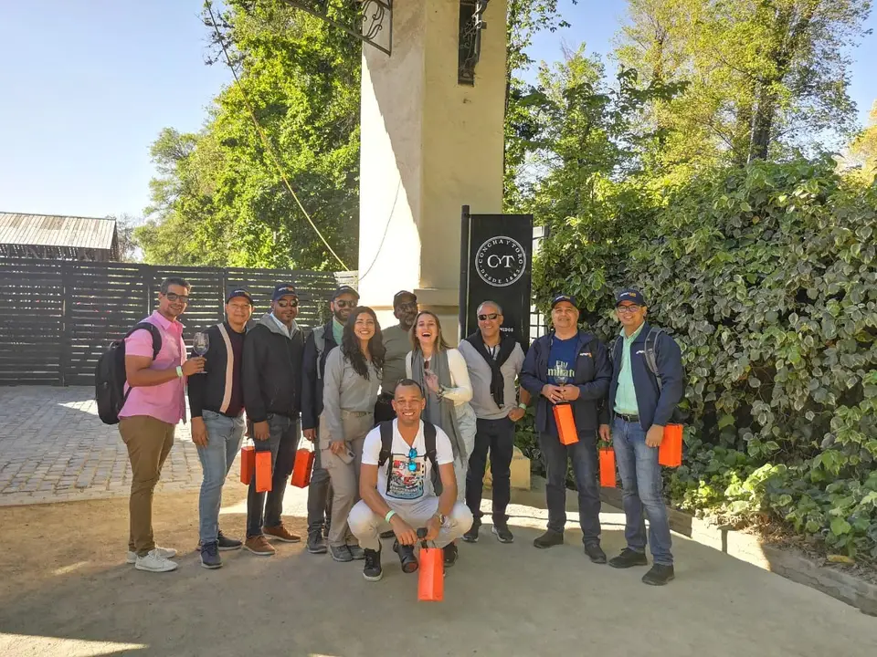 Grupo de visitantes posando junto a la entrada de una viña, con bolsas naranjas en las manos