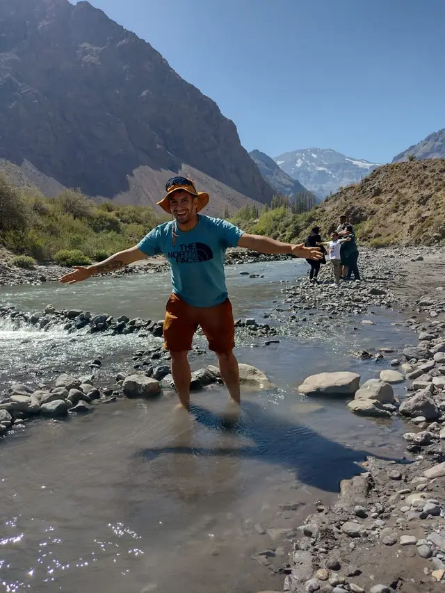 Excursionista con los brazos abiertos dentro de un río de montaña en el Cajón del Maipo