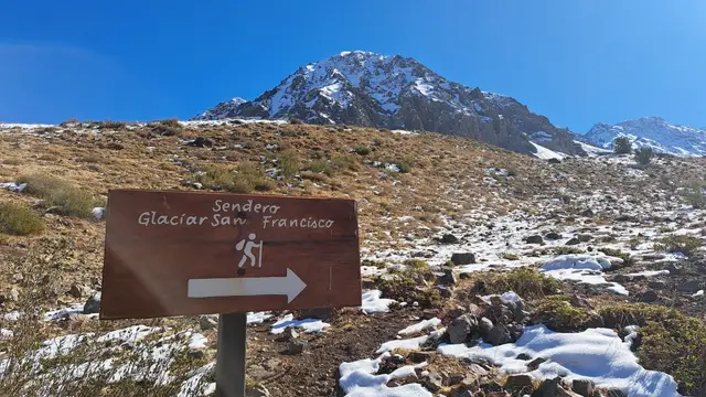 Cartel del sendero al Glaciar San Francisco en el Monumento Natural El Morado, con la montaña nevada detrás