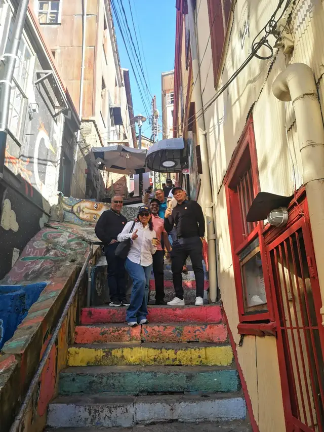 Pasaje con escalones pintados de colores y murales en un cerro de Valparaíso, con un grupo de viajeros